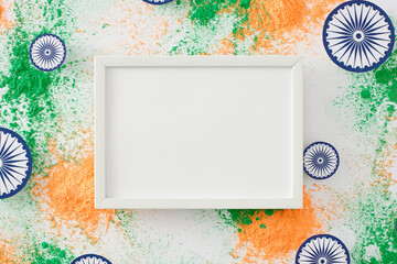 Happy India Republic Day theme. Top view flat lay of green and saffron holi powder, ashoka wheels on white background with empty frame for promo or text