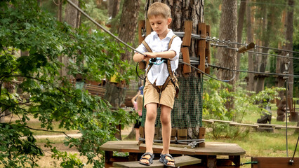 Poster - Little concentrated boy lookin down his feet while crossing rope bridge in extreme park