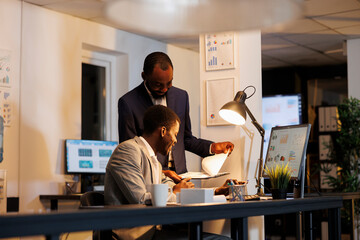 African american men analyzing financial statistics typing company strategy on computer, discussing investment growth report. Executive managers working late at night in startup office