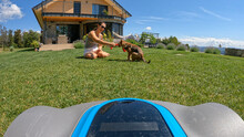 POV = POINT OF VIEW: Autonomous Lawnmower Approaching Playful Woman And Her Dog