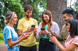 © unai - Multiethnic group smiling with phones on internet or social networks in the park, technology concept