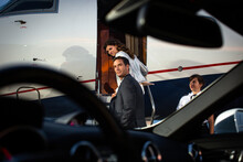 Successful Couple Boarding Private Jet , Man Looking Back Over Shoulder On Tarmac Of Airport, View From Drivers Seat Of Sports Car Parked Next To Plane On Tarmac 