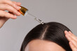 © New Africa - Woman applying essential oil onto hair roots on light grey background, closeup