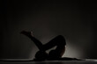 © Nikola Spasenoski - Fit ballerina girl lying and stretching practicing yoga poses. Side lit silhouette against dark background.. .