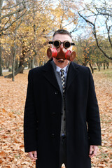 Wall Mural - Man in black coat, business suit and gas mask posing in autumn park