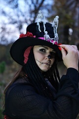 Wall Mural - A woman dressed as Baron Saturday poses for the camera. The model is dressed in a corset, a cardigan and a cylinder hat decorated with skeleton figures.