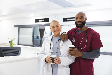 Wall Mural - Portrait of happy diverse male and female doctors holding takeaway coffee in reception at hospital