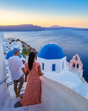 Couple Watching The Sunset On Vacation In Santorini Greece, Men And Women Visit The Greek Village Of Oia Santorini.