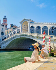 Wall Mural - a couple of men and women on a city trip in Venice Italy sitting at the waterfront of the Rialto bridge in Venice, Italy.