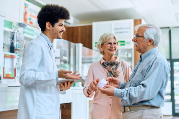 Wall Mural - Happy pharmacist assists senior couple with choosing vitamins in pharmacy.