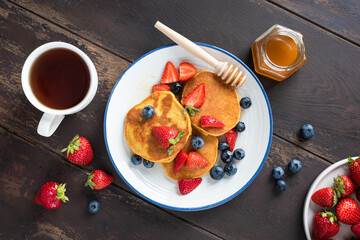 Wall Mural - Pancakes with berries and honey on wooden table, top view. Sweet breakfast or brunch meal