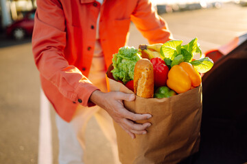 Wall Mural - Young man with a bag full of groceries, in a car. Grocery delivery man prepares fresh vegetable delivery service. Healthy lifestyle.