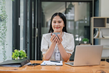 Sticker - Beautiful young smiling Asian businesswoman working on laptop and drinking coffee, Asia businesswoman working document finance in office