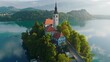 Flying around small island on Bled Lake in Slovenia. Aerial view of Church of the Assumption of Mary in the center of the lake Bled. Warm morning sun and light fog