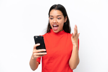 Wall Mural - Young Colombian woman isolated on white background looking at the camera while using the mobile with surprised expression