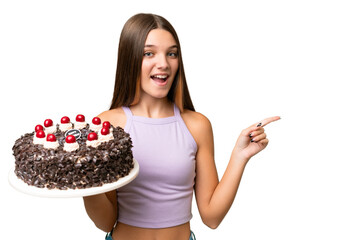 Wall Mural - Teenager caucasian girl holding birthday cake over isolated background surprised and pointing finger to the side