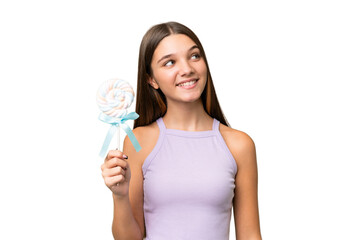 Sticker - Teenager caucasian girl holding a lollipop over isolated background looking up while smiling