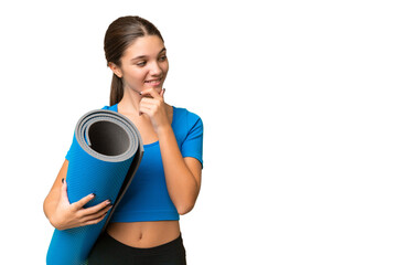 Wall Mural - Teenager caucasian girl going to yoga classes while holding a mat over isolated background thinking an idea and looking side