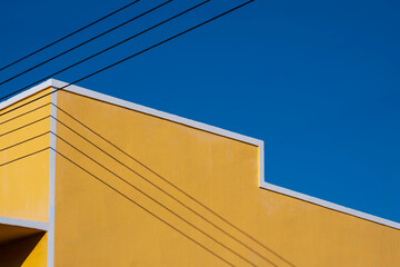 the old vintage yellow house wall with electric cable lines against blue clear sky background, low a