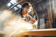 © Goffkein - Strong woman carpenter working with circular saw on wooden plank in workshop. Craftswoman with successful small business, women's equality