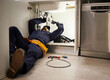© Malik/peopleimages.com - Kitchen, maintenance and renovation with a plumber on the floor of a home to fix a leak, issue or problem. Plumbing, repair and tools with a handyman or contractor working on a pipeline in a house