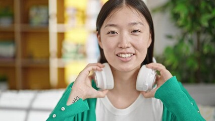 Poster - Young chinese woman listening to music sitting on sofa at home