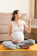 © sosiukin - Pregnant young woman with bottle of water while sitting in lotus position on yoga mat. Maintaining water balance at coronavirus time