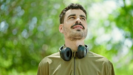 Sticker - Young hispanic man smiling confident wearing headphones breathing at park