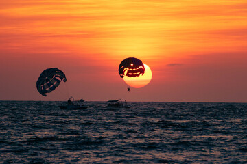 Silhouette of people parasailing in the sea at sunset time.