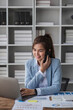 © wichayada - Portrait of young business woman with sitting in office in front of her laptop and talking on mobile phone hand at office