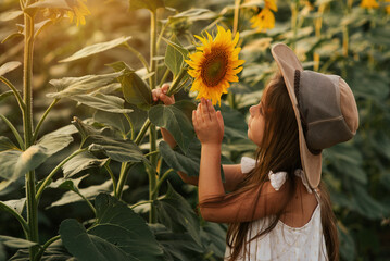 happy cute little girl in the hat on the field of sunflowers in summer. happy childhood