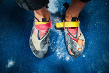 Closeup Of A Man's Climbing Shoes With Toes Poking Out Against A Blue Chalk Dusted Mat In A Climbing Gym