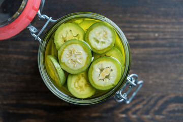 Wall Mural - Sliced unripe walnuts in alcohol in a jar, to prepare homemade tincture, closeup. Tincture of green walnuts in a glass jar on a wooden table, top view