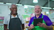 © Marco - Joyful diverse Brazilian senior staff workers of supermarket chain smiling at camera with table and uniforms. African American older employee and a caucasian person laughing together