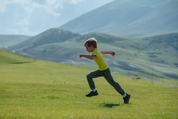 Wall Mural - Boy running fast on a green meadow in the mountains