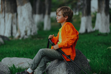 Poster - Boy hiker with trekking poles sitting on a boulder and looking away