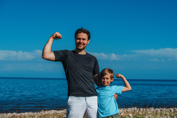 Canvas Print - Happy father and son showing their muscles on the beach