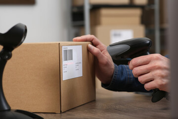 Canvas Print - Seller with scanner reading parcel barcode at table in office, closeup. Online store