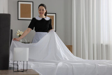 Wall Mural - Young maid making bed in hotel room. Space for text