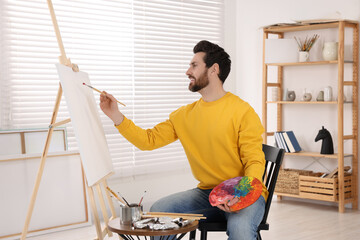 Poster - Man painting in studio. Using easel to hold canvas