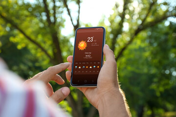 Wall Mural - man checking weather using app on smartphone outdoors, closeup. data, sun and other illustrations on