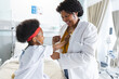 African american female doctor playing with girl patient using stethoscope at hospital