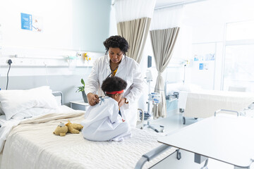 Wall Mural - African american female doctor examining girl patient using stethoscope at hospital