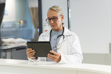 Wall Mural - Senior caucasian female doctor wearing lab coat using tablet in reception at hospital