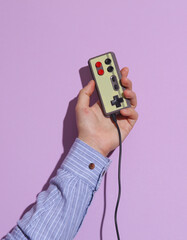 Wall Mural - Man's hand in shirt holding retro joystick on purple pastel background with shadow.