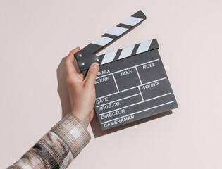 Wall Mural - Man's hand in shirt holding clapperboard on beige pastel background with shadow.