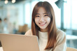 © Surachetsh - A Smiling Asian Woman working with her laptop in front of light cream background. generative AI.