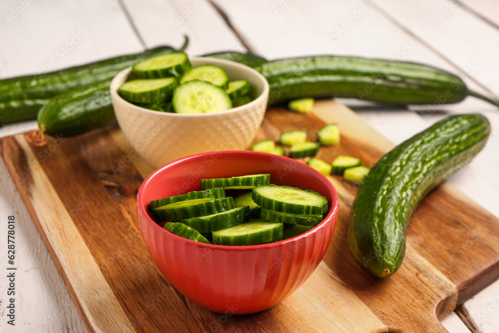 Board with fresh cucumbers on light wooden background, closeup