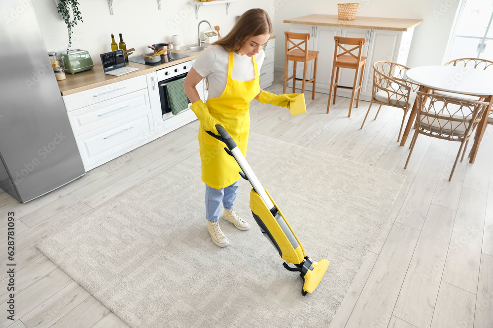 Young woman with rag vacuuming carpet in kitchen