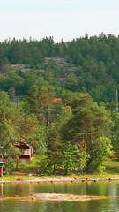 Wall Mural - Vertical Footage Video. Many Red Swedish Wooden Sauna Logs Cabins Houses On Island Coast In Summer Cloudy Day.